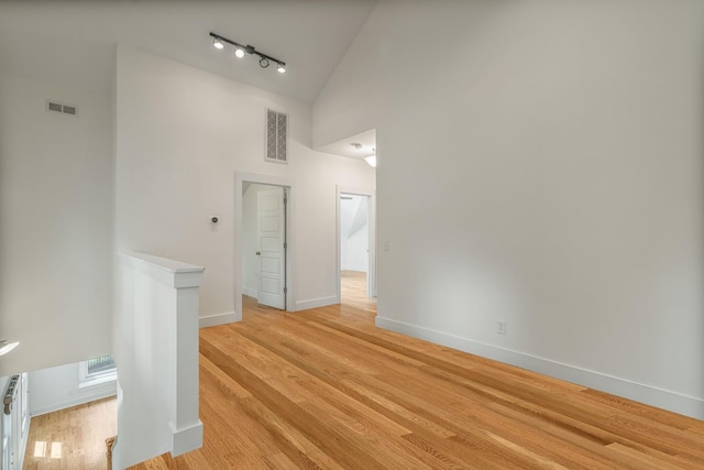 empty room featuring light wood-type flooring, track lighting, and high vaulted ceiling