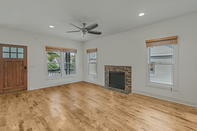 unfurnished living room featuring light hardwood / wood-style flooring, a stone fireplace, and ceiling fan