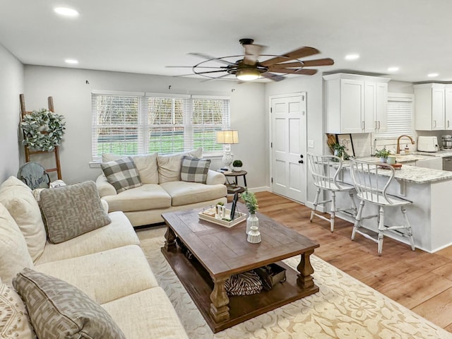 living room featuring light wood-type flooring, ceiling fan, and sink