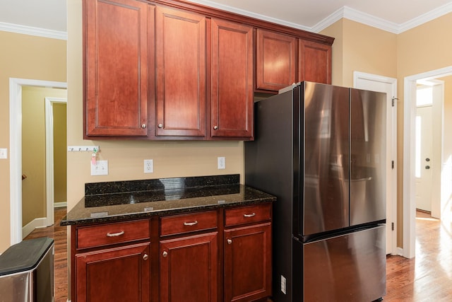 kitchen with ornamental molding, light wood-type flooring, dark stone countertops, and stainless steel refrigerator