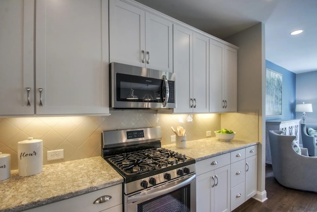 kitchen with stainless steel appliances, tasteful backsplash, light stone countertops, white cabinets, and dark hardwood / wood-style flooring