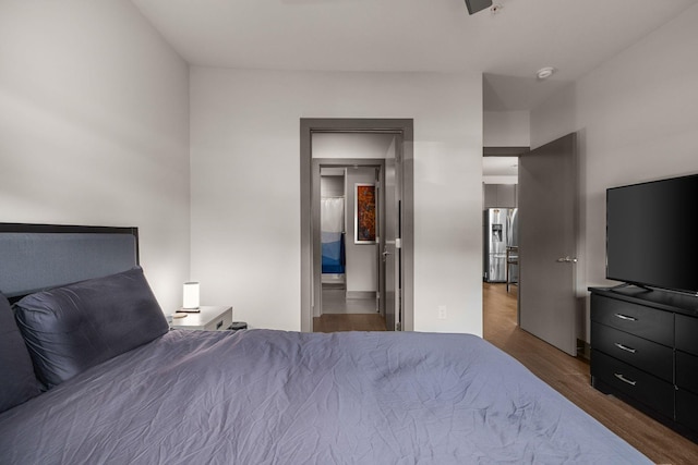 bedroom featuring hardwood / wood-style flooring, stainless steel fridge, and connected bathroom