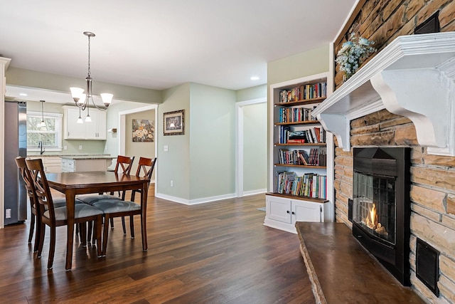 dining area with an inviting chandelier, a stone fireplace, sink, built in shelves, and dark hardwood / wood-style floors