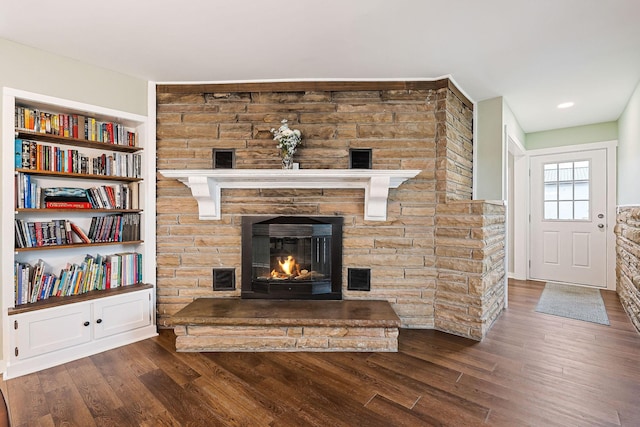 living room featuring built in features, dark hardwood / wood-style flooring, and a stone fireplace