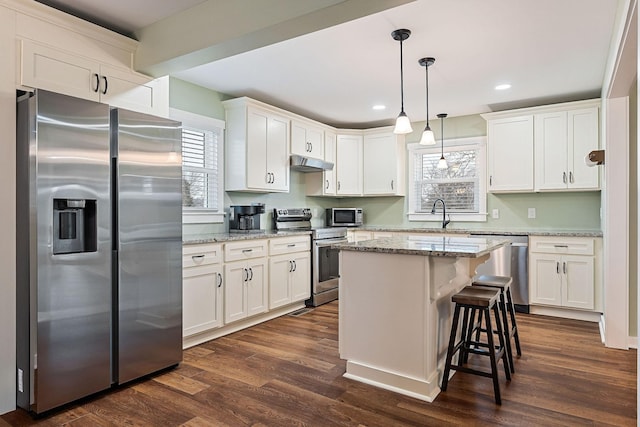 kitchen featuring stainless steel appliances, a kitchen island, hanging light fixtures, and light stone counters