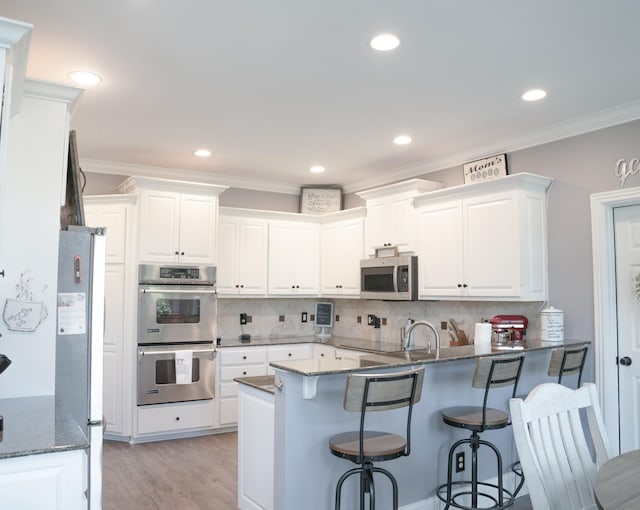 kitchen featuring white cabinets, ornamental molding, tasteful backsplash, kitchen peninsula, and stainless steel appliances