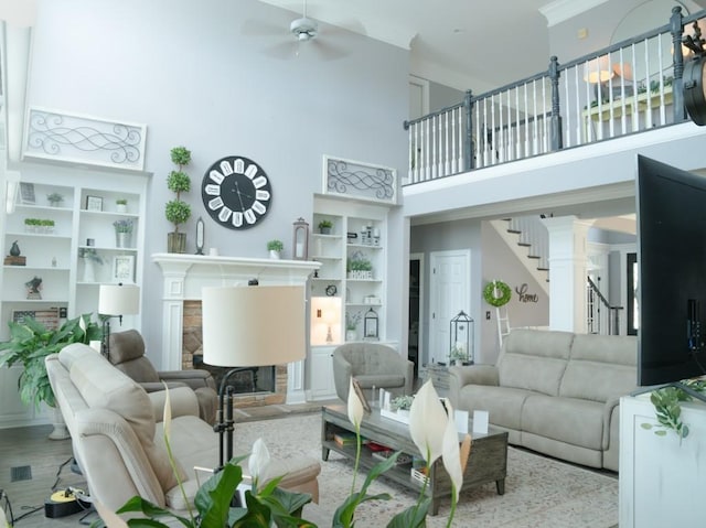 living room featuring light wood-type flooring, a towering ceiling, ceiling fan, built in features, and a stone fireplace