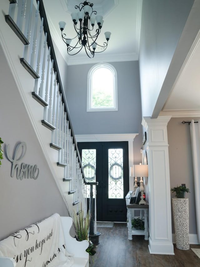 foyer entrance featuring french doors, ornamental molding, a towering ceiling, dark hardwood / wood-style flooring, and a chandelier