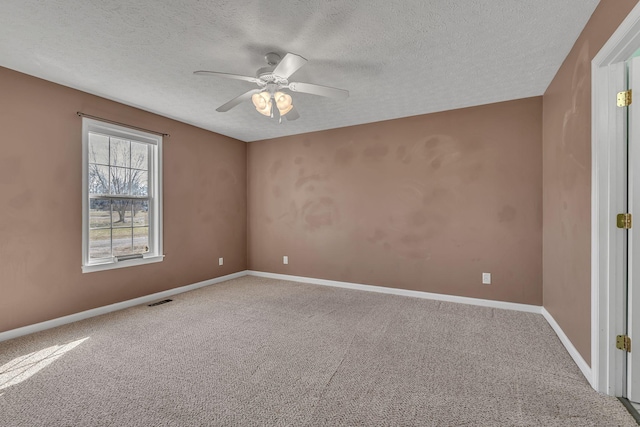 empty room with visible vents, a textured ceiling, carpet flooring, baseboards, and ceiling fan