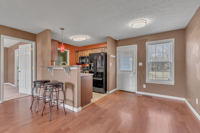 kitchen featuring a breakfast bar area, light wood-style flooring, a peninsula, a textured ceiling, and black appliances