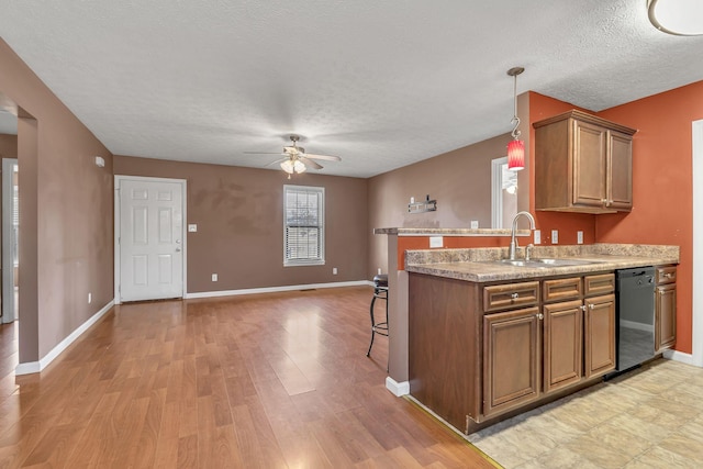 kitchen featuring baseboards, light wood finished floors, a sink, dishwasher, and brown cabinets