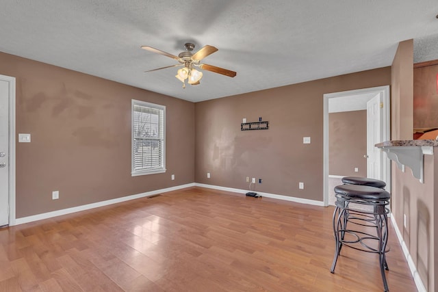 empty room featuring light wood-type flooring, baseboards, a textured ceiling, and a ceiling fan