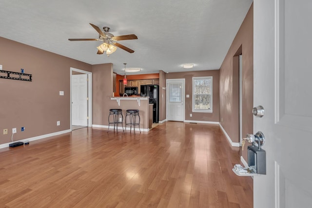 unfurnished living room with light wood-type flooring, baseboards, a textured ceiling, and a ceiling fan