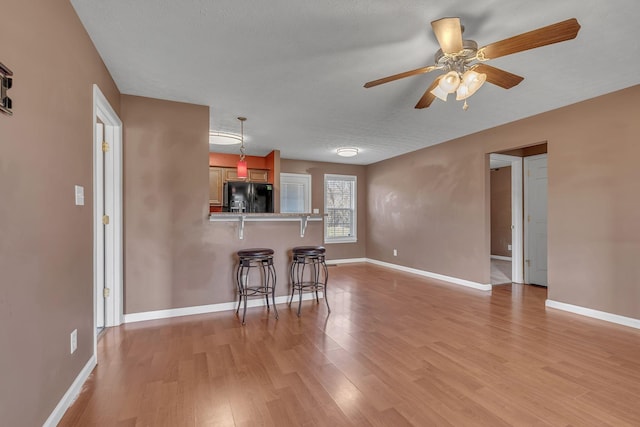 kitchen with a breakfast bar, black fridge with ice dispenser, light wood-style floors, a peninsula, and baseboards