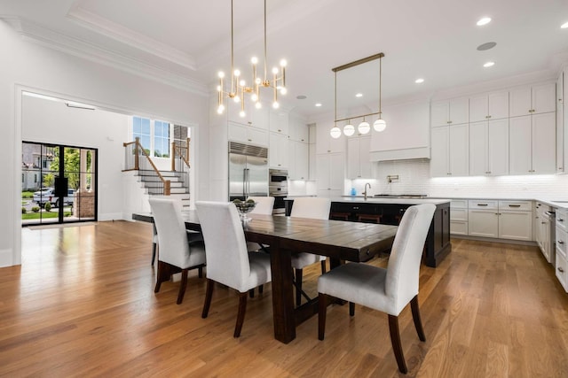 dining area with sink, ornamental molding, a notable chandelier, and light wood-type flooring