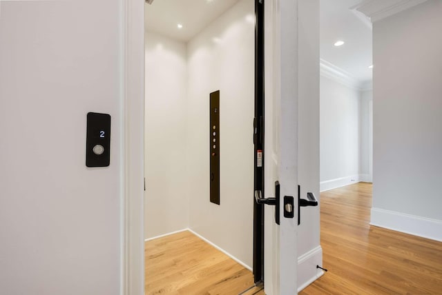 hallway featuring elevator, crown molding, and light hardwood / wood-style flooring