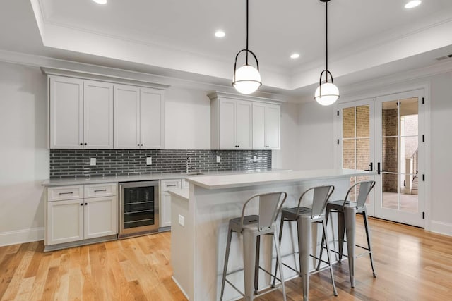 kitchen with a center island, a raised ceiling, hanging light fixtures, and wine cooler