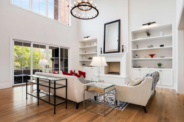 living room featuring hardwood / wood-style floors, built in shelves, a high ceiling, and an inviting chandelier