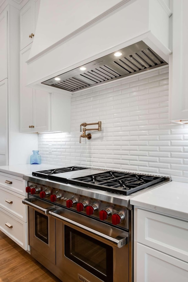 kitchen with backsplash, range with two ovens, white cabinets, custom range hood, and light wood-type flooring