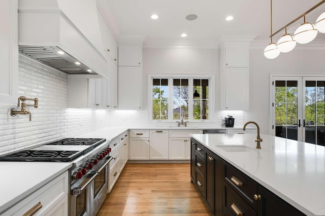 kitchen featuring custom exhaust hood, sink, range with two ovens, white cabinets, and hanging light fixtures