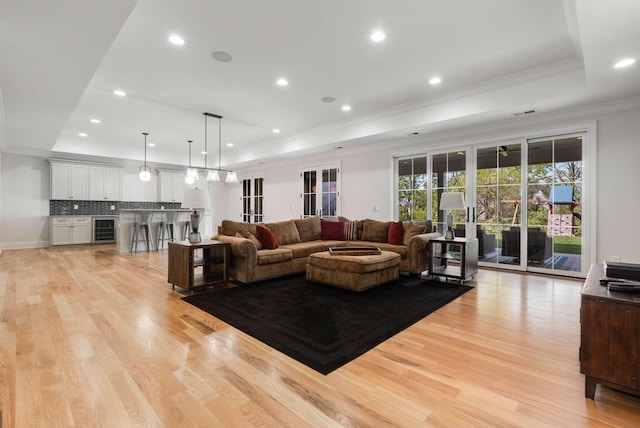 living room with ornamental molding, a tray ceiling, beverage cooler, and light hardwood / wood-style floors