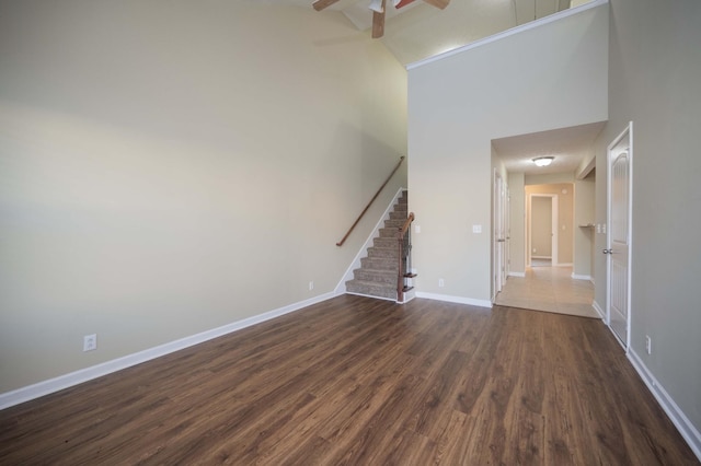 unfurnished living room featuring ceiling fan, dark hardwood / wood-style flooring, and a towering ceiling