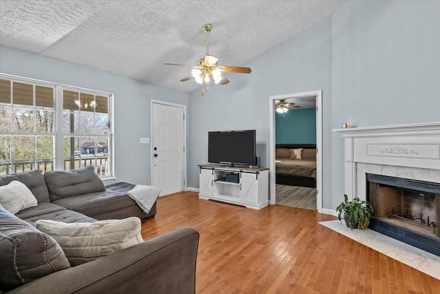 living room with ceiling fan, wood-type flooring, a textured ceiling, and vaulted ceiling