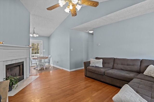 living room featuring hardwood / wood-style flooring, vaulted ceiling, a textured ceiling, ceiling fan with notable chandelier, and a tile fireplace