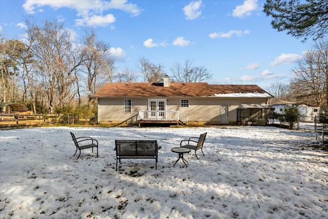 snow covered back of property with a deck and french doors