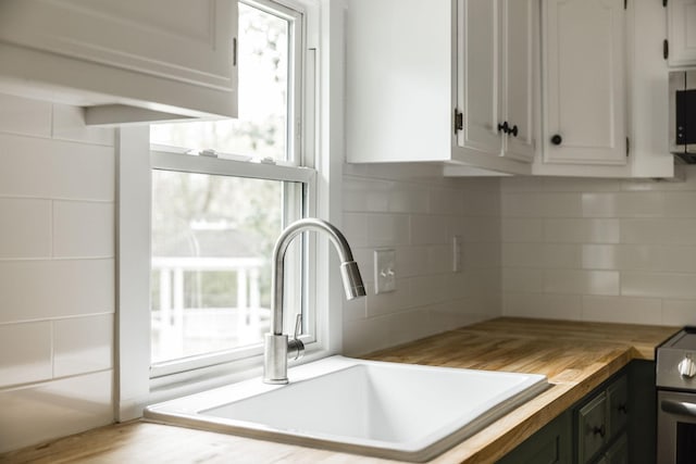 kitchen with butcher block countertops, decorative backsplash, white cabinets, and sink