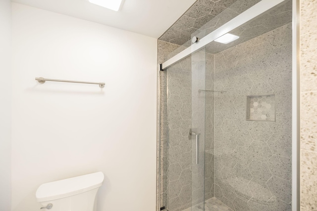 bathroom featuring a shower with door and toilet