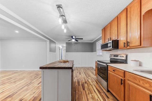 kitchen featuring appliances with stainless steel finishes, ornamental molding, light hardwood / wood-style flooring, butcher block countertops, and a kitchen island