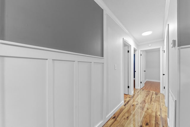 hall with light wood-type flooring and ornamental molding