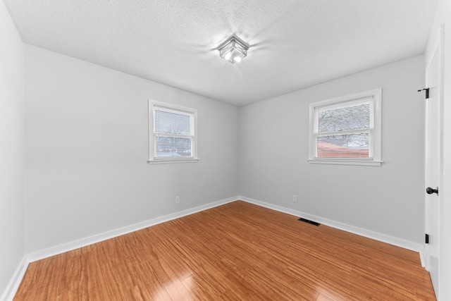 empty room with hardwood / wood-style flooring, a textured ceiling, and a wealth of natural light