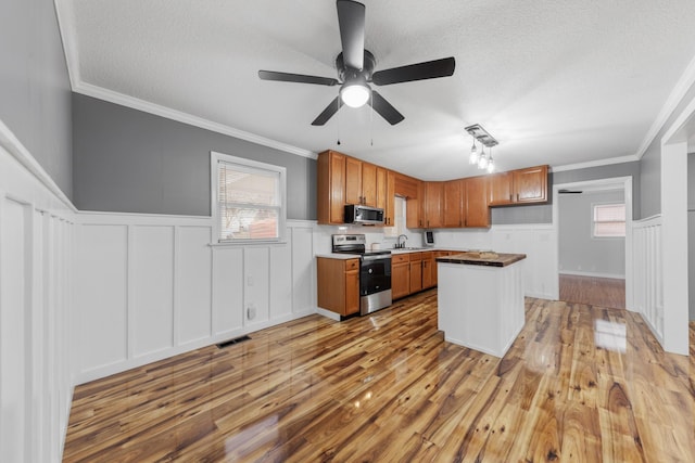 kitchen with appliances with stainless steel finishes, ornamental molding, a textured ceiling, sink, and hardwood / wood-style flooring