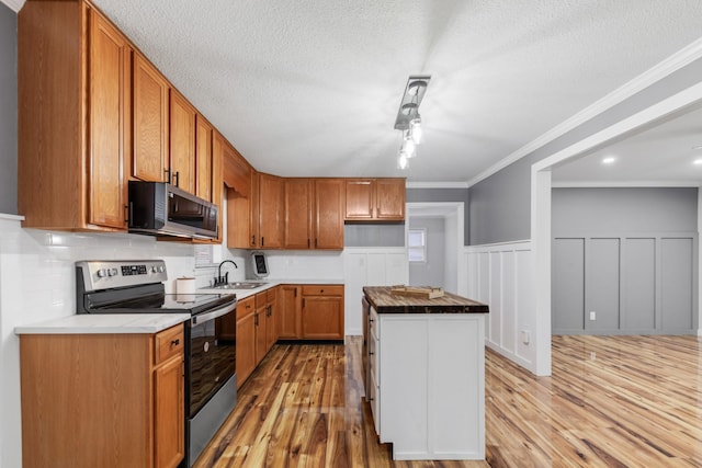 kitchen with sink, ornamental molding, a textured ceiling, appliances with stainless steel finishes, and light hardwood / wood-style floors