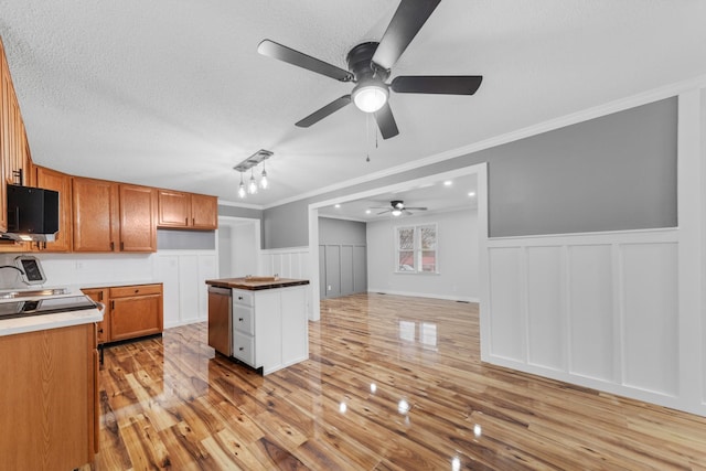 kitchen featuring a center island, stainless steel dishwasher, light wood-type flooring, ornamental molding, and a textured ceiling