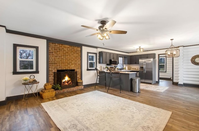 living room featuring ceiling fan with notable chandelier, crown molding, sink, a fireplace, and dark hardwood / wood-style floors