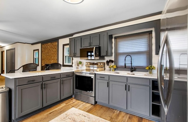 kitchen with kitchen peninsula, stainless steel appliances, crown molding, sink, and light hardwood / wood-style floors