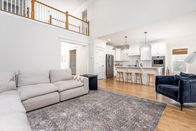 living room with a high ceiling, light hardwood / wood-style floors, ornamental molding, and sink