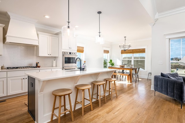 kitchen with premium range hood, pendant lighting, a center island with sink, white cabinets, and appliances with stainless steel finishes