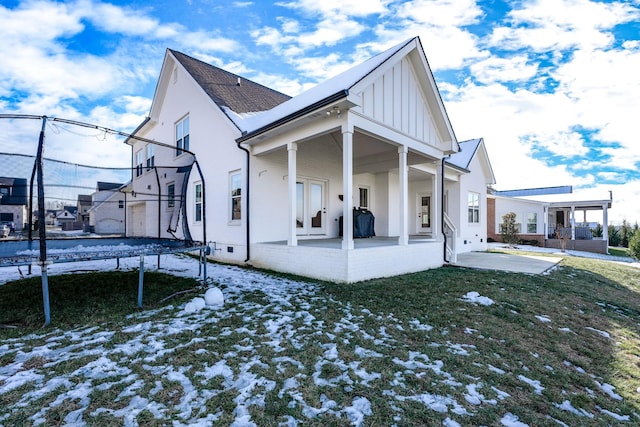 snow covered rear of property featuring a lawn, a trampoline, and a patio