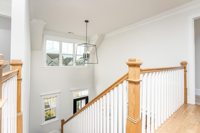 staircase featuring hardwood / wood-style floors, crown molding, and an inviting chandelier