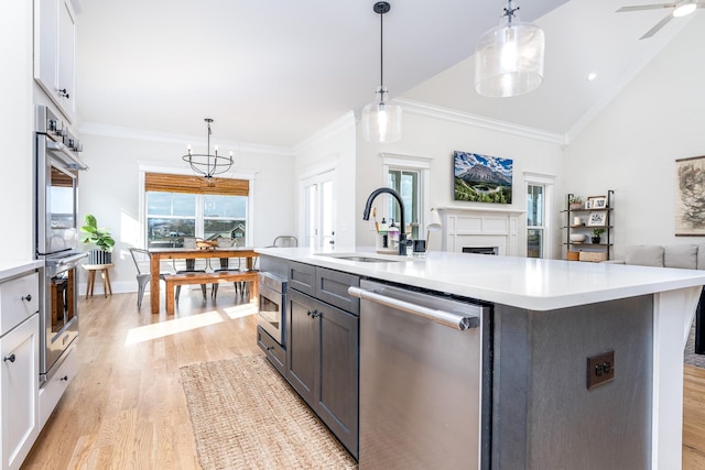 kitchen featuring appliances with stainless steel finishes, pendant lighting, light hardwood / wood-style flooring, white cabinets, and an island with sink