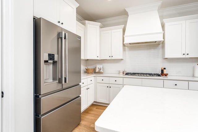 kitchen featuring custom exhaust hood, backsplash, light hardwood / wood-style flooring, appliances with stainless steel finishes, and white cabinetry