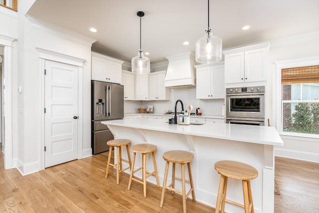 kitchen featuring white cabinetry, light hardwood / wood-style floors, a center island with sink, custom range hood, and appliances with stainless steel finishes