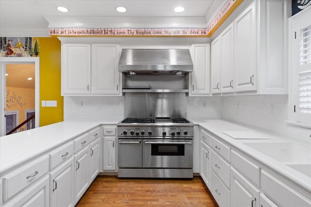 kitchen with wall chimney exhaust hood, light hardwood / wood-style flooring, ornamental molding, double oven range, and white cabinets