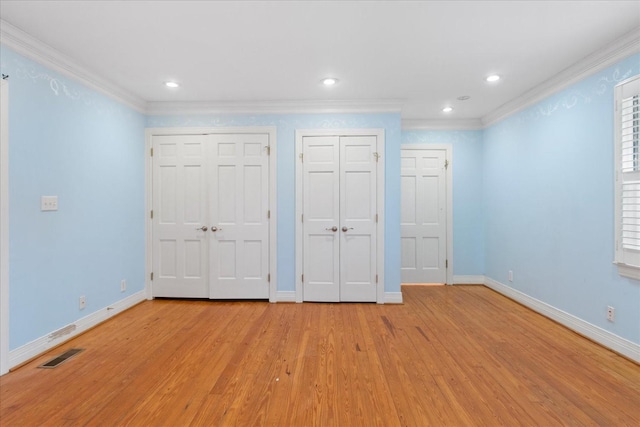 unfurnished bedroom with crown molding, light hardwood / wood-style floors, and two closets