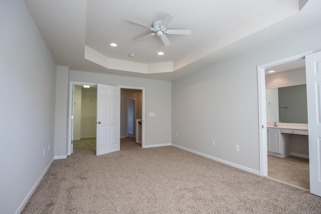 unfurnished bedroom featuring connected bathroom, a tray ceiling, a spacious closet, and light colored carpet