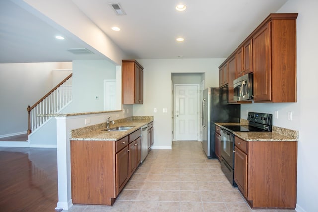 kitchen with kitchen peninsula, appliances with stainless steel finishes, light stone counters, sink, and light tile patterned floors